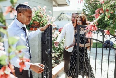 Mężczyzna W Białej Koszuli I Czarno Białych Spodniach W Kropki, Trzymając Się Za Ręce Z Kobietą - Fot. Kindel Media